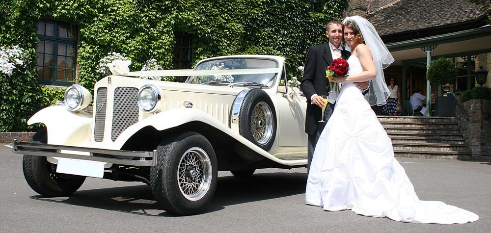 Bride and groom beside the ivory Beauford open top tourer outside an ivy-clad venue