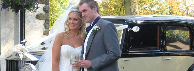 Bride and groom with champagne beside a classic wedding car