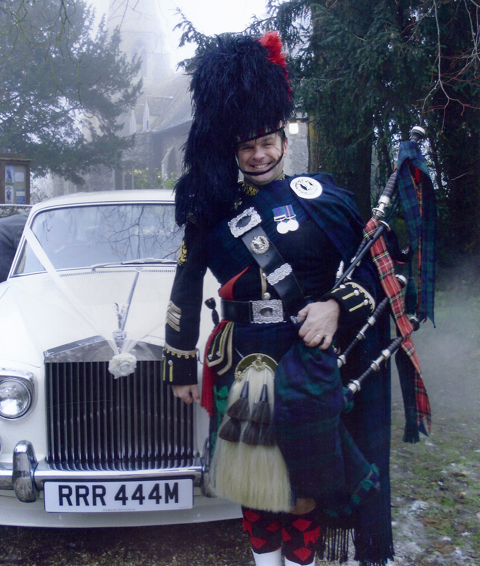 Piper in full dress beside an ivory Rolls Royce outside a church