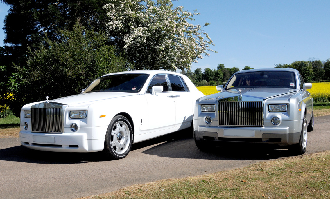 White and silver Rolls Royce Phantom wedding cars parked on a country lane