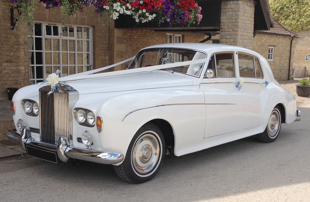 Ivory Rolls Royce Silver Cloud III wedding car dressed with ribbon outside a stone venue